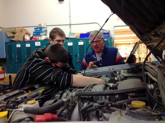 Jacob Alvey, Joe Harris, and David Sweetman look under the hood of a car in the auto shop.