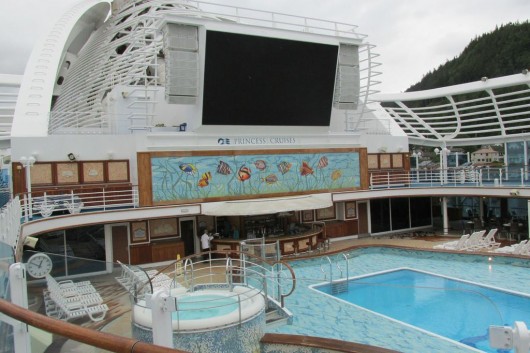 A pool with a movie screen hovering above it on the Crown Princess.