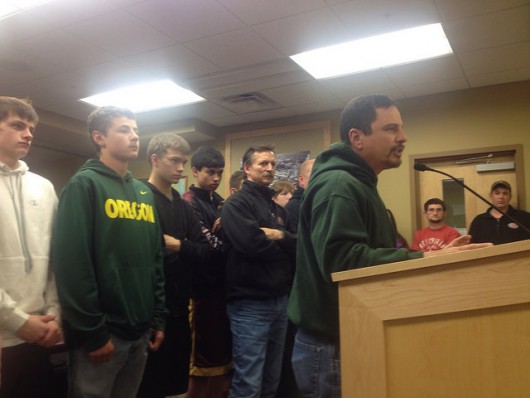 Former Kayhi football coach Les Silva talks to the Ketchikan School Board with football players standing behind him.