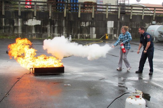 KRBD's intern, Megan Petersen, practices putting out a controlled fire with an extinguisher.
