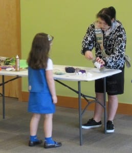 Girl Scout Nayomie Welty helps a young girl make a cat toy.