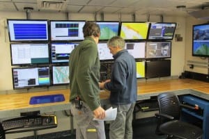 Capt. Adam Seamans and Steve Roberts stand in front of a wall of computer screens on board the ocean research vessel Sikuliaq.
