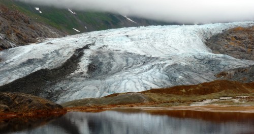 A glacier reflects in a naturally occurring pool of rusty, acidic water at the site of one of the KSM Prospect's planned open-pit mines. The British Columbia project, northeast of Ketchikan, is drilling for higher-value ore this summer. (Photo by Ed Schoenfeld/CoastAlaska News)