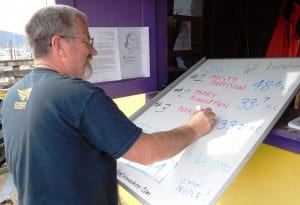 Lions Club volunteer Glenn Brown changes the leader whiteboard at the Bar Harbor weigh-in station Sunday afternoon.  (Ed Schoenfeld/CoastAlaska News)