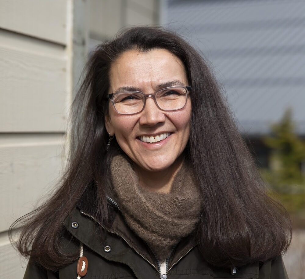 a woman with dark hair and glasses smiles outside a building