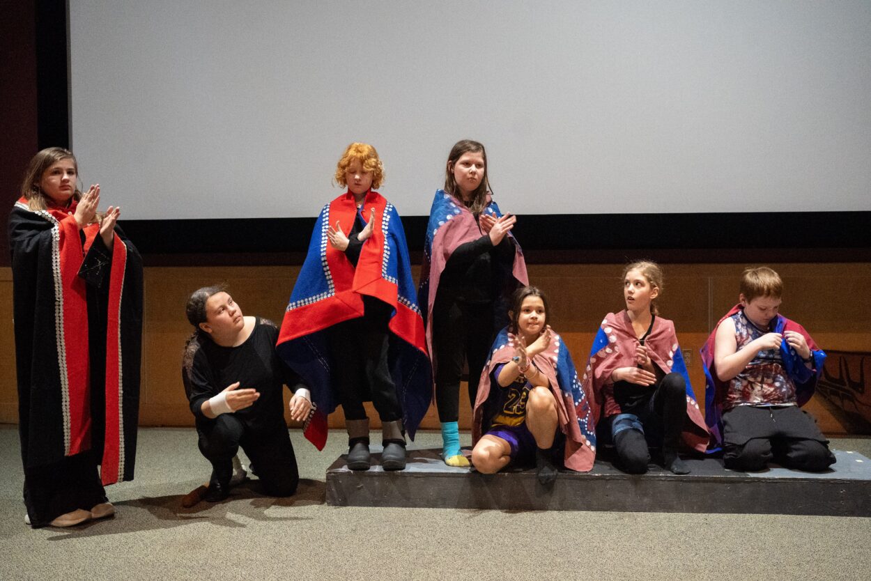 students in traditional costumes act out a play on a stage