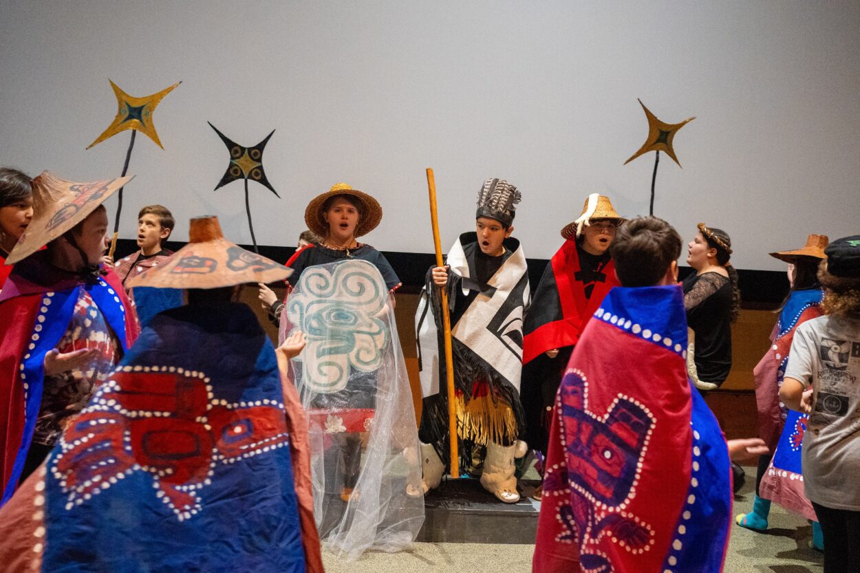 children in costumes with props, singing and dancing on a stage