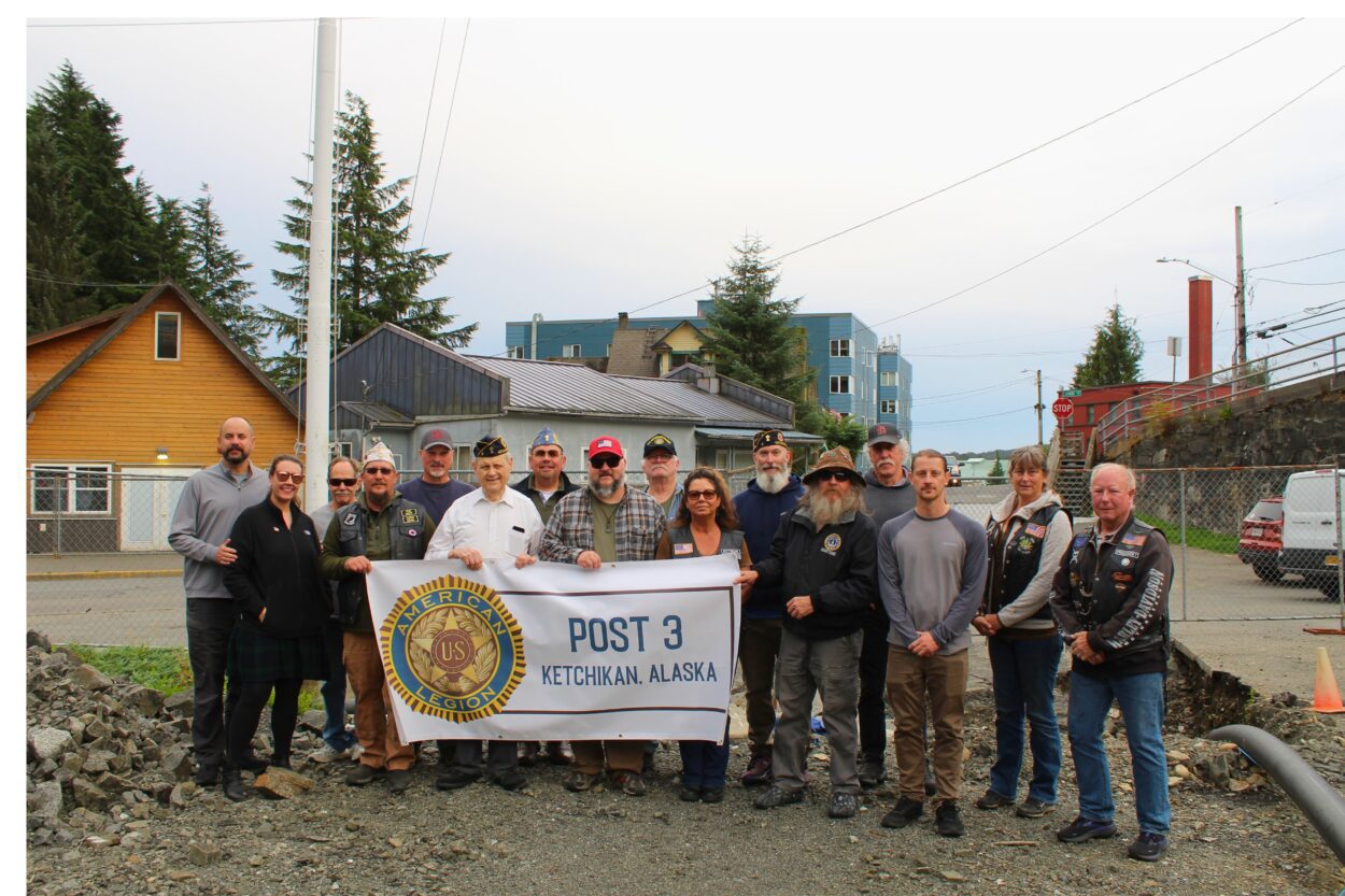 a group of 16 people pose with a sign that reads "Post 3, Ketchikan, Alaska"