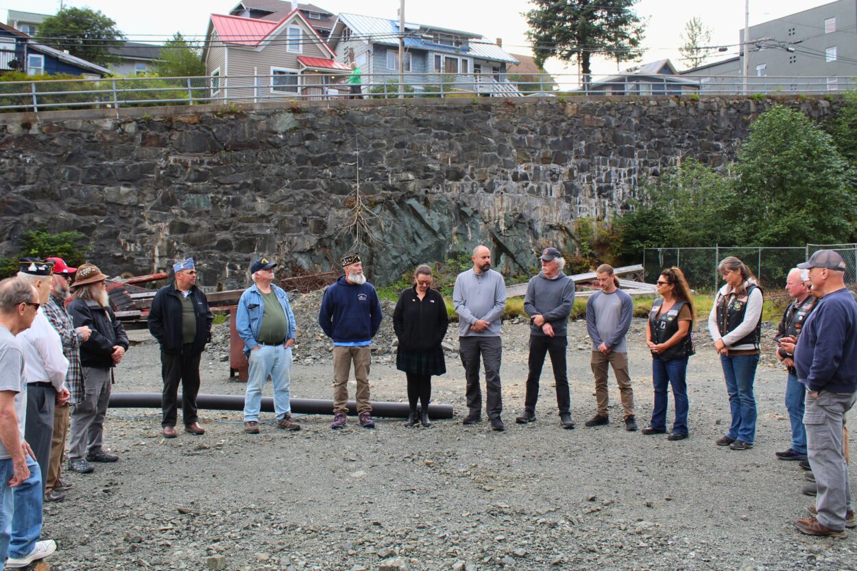 a group of people stand in a semi-circle on an open plot of land