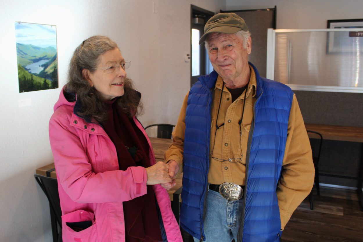 a woman and man smiling, shaking hands in an indoor space